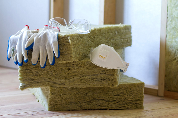 Pile de matériaux isolants avec masque, gants et lunettes de protection posés dessus