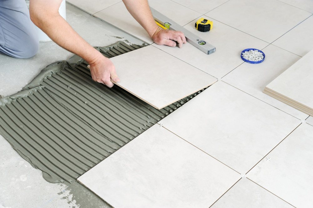 Pose de carrelage au sol avec colle à carrelage, artisan en train d’installer un carreau en céramique sur chape fraîche