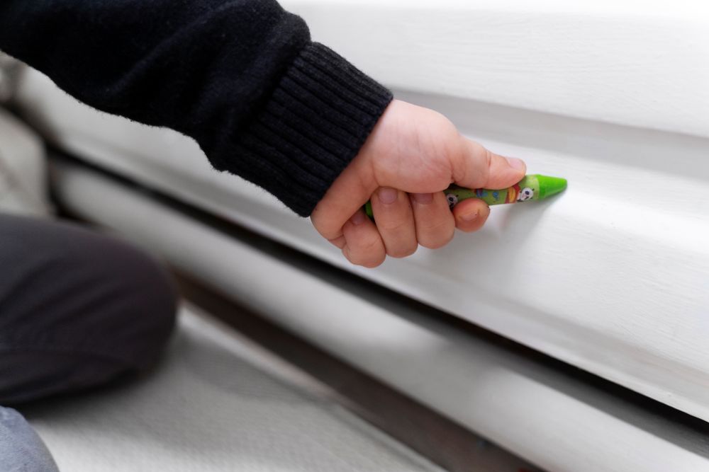 Zoom sur une main d'enfant qui qui dessine sur chauffage par plinthe